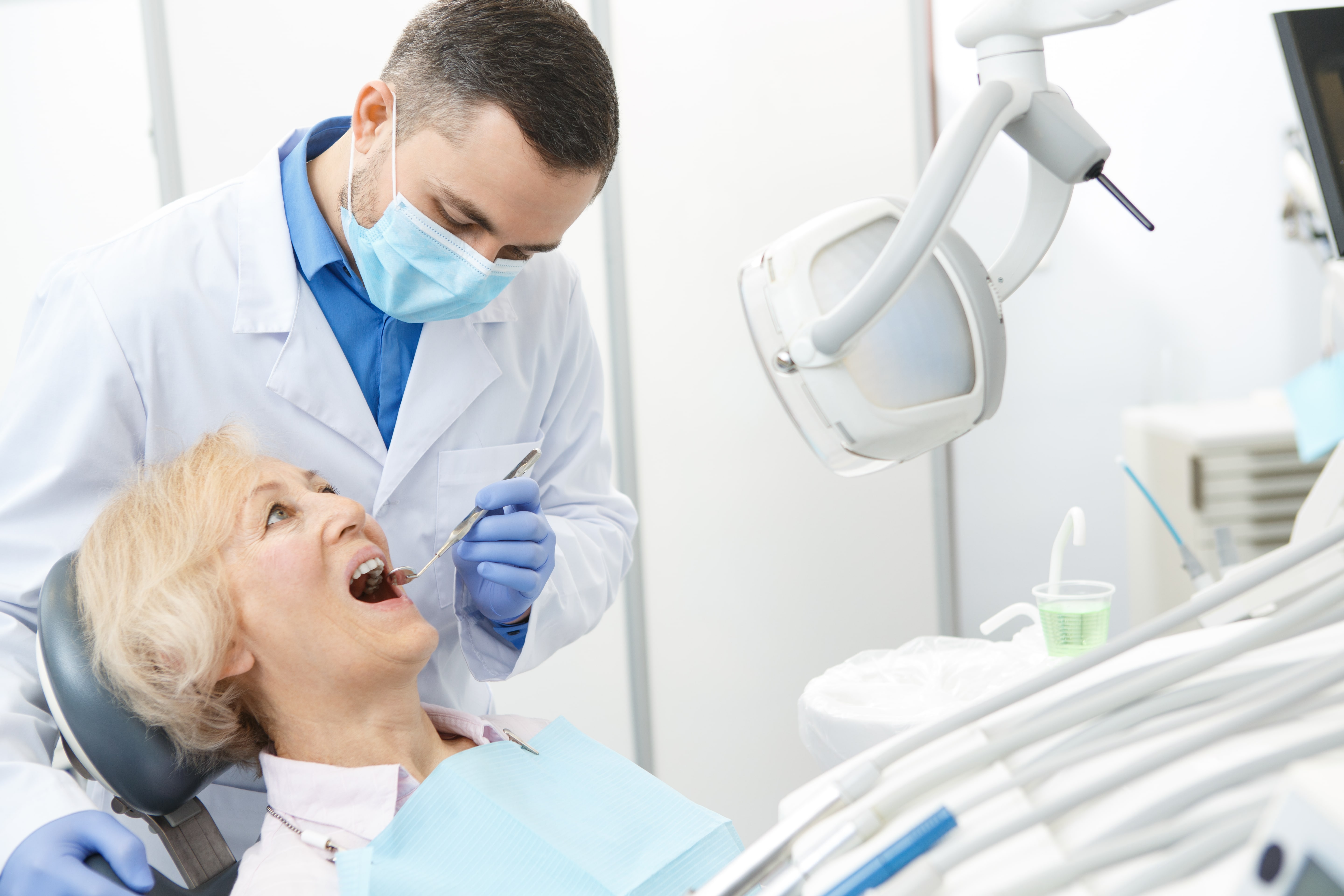 Врач занимающийся протезированием зубов. Стоматолог и пациент. Осмотр стоматолога. Пациент на приеме у стоматолога.